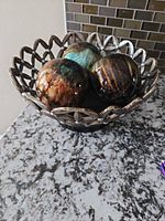 Metal lattice bowl holding three glazed ceramic spheres on countertop