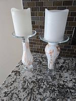 Two clear glass candlestick holders with flameless candles displayed on countertop