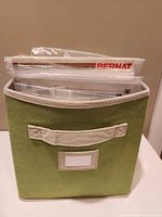 Front view of green fabric bin filled with craft kits and magazines