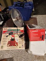 Boxed Supreme tree stand, Lasko heater box, Presto HeatDish heater and blue stadium cushions stacked