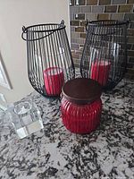 Two black wire lanterns with red candles, red jar candle, clear cube tealight holder