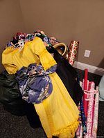 Pile showing yellow dress, black garment, blue floral tote, some hats and gift-wrap rolls