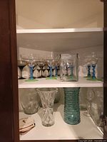 Cabinet shelf with colored-stem cocktail glasses, smoked wine glasses, square jar, crystal and aqua vases