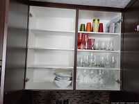 Open cabinet showing all shelves with glassware, plastic tumblers, bowls and plates