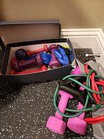 Overview of box with assorted neoprene dumbbells, blue ankle/wrist weights and resistance bands on floor