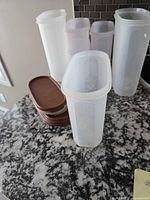 Group of tall translucent containers and stacked lids on countertop