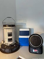 Group view of Coleman ProCat heater, kerosene heater, two blue coolers
