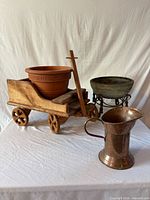 Group view of copper pitcher, wooden wagon plant stand with terracotta pot, and stoneware planter on iron stand