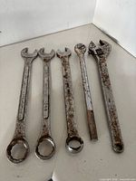 Group of four large combination wrenches and one 24-in adjustable wrench laid side by side