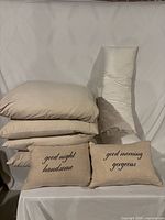Stack of four beige square pillows, white body pillow, two beige lumbar decorative pillows