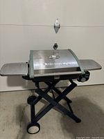 Grill set up on stand showing full front view with side shelves and control knob