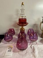 Decanter on pedestal bowl with six amethyst glasses visible