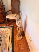 Full view of plaster classical female statue beside chair for scale
