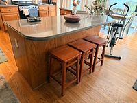 Three solid wood backless stools under kitchen island showing shape, size, and finish