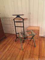Four housekeeping aids: black valet stand with wheels, woven wood hamper, green folding luggage stand, and light wood folding drying rack on a wooden floor