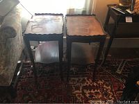 Two vintage wooden side tables placed side by side next to a sofa, showing their overall shape and size with pie crust scalloped edges on the tabletop and lower shelves.