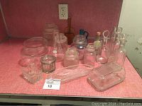 Various clear glass containers, jars and bottles with lids and stoppers, arranged on red shelf surface under electrical outlet.
