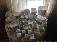 Lot of over 50 white china serving and tableware items arranged on a table, including a variety of cups, bowls, ramekins, rectangular baking dishes, and casseroles.