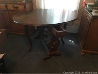 Opened oval-shaped vintage gateleg table with one drawer open, showing ornamental legs and wood grain.