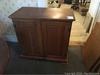 Front view of the closed pine side cabinet showing two paneled doors and base with some signs of wear.