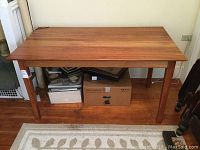 Full view of cherry library table showing rectangular top and four legs. Table is standing on a rug with visible under-table storage boxes around.