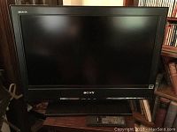 Full view of Sony Bravia flat screen TV on stand with remote placed in front of it on wooden surface.