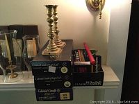 Photo of brass beehive candlesticks and several boxed candles stacked together along with a loose red candle