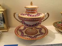 Covered dish with lid and saucer, gold background with pink floral garlands and cherub decoration on footed cup visible