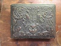Top view of tooled leather box with twin griffins and decorative scrollwork.
