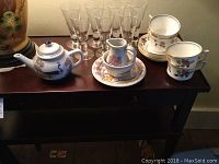 Overall display of teapot, creamer, sugar bowl, six clear shrub glasses, and four cups with saucers.