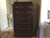 Full view of the tall mahogany bureau with six graduated drawers featuring brass North Wind pulls and carved Eastlake style detailing on edges and corners.
