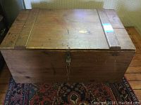 Front view of pine wood lidded box with visible padlock and key attached, showing some paint splashes on top surface and two horizontal wood panels on lid.