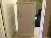 Front view of the white metal cabinet with closed door, showing metal handle and slight chipping at top corner.