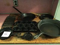 Seven-seasoned pans arranged on a wooden surface including multiple cast iron and aluminum pans.