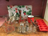 Full lot arranged showing measuring cups, mixing bowl with spoons, salt and pepper shakers, metal shaker, glass creamer, enamel mug, ceramic geranium tray, and red silicone ice cube trays.