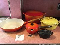 Five pieces of vintage Le Creuset cookware on shelf, showing colors and wear.