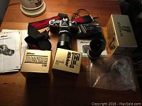 Overview on wood table showing F3 camera body mounted with telephoto lens, lens boxes (TC-200, 50 mm), strap, manuals and pixel accessory