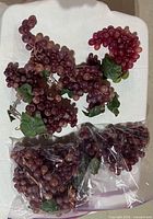 Group of faux grape bunches loose and in zipper bags on table