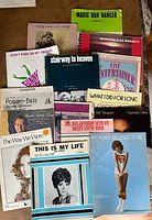 Assortment of sheet music pieces spread on tabletop including Music Box Dancer, Stairway to Heaven, The Entertainer and others