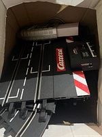 Box containing straight track sections with red-white curb graphics, electronic control unit and wired controller