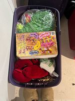 Overview of bin showing grass skirt, Mega Lei box, red plush pieces, green bag
