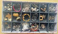 Overview of entire compartmented box filled with mixed jewelry pieces