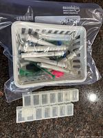 Basket containing multiple syringes sealed in a plastic bag, two 12-compartment storage boxes