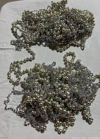 Two piles of mixed silver and pearl plastic bead garlands