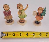 Front view of all three Goebel Hummel figurines with ruler for scale