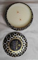 Voluspa Tuberosa Di Notte tin candle open showing white wax and two wicks with patterned lid beside