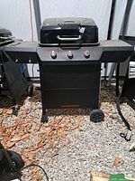 Front view of Megamaster black 3-burner propane grill showing side shelves and wheels