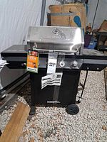 Front angled view of Nexgrill grill showing stainless lid, side shelves, wheeled cart and tags