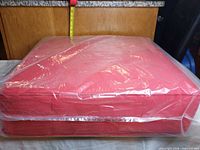 Red cushion sealed in plastic, side view shows boxed edges