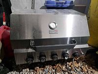 Front view of stainless grill head showing lid, thermometer, handle and five control knobs